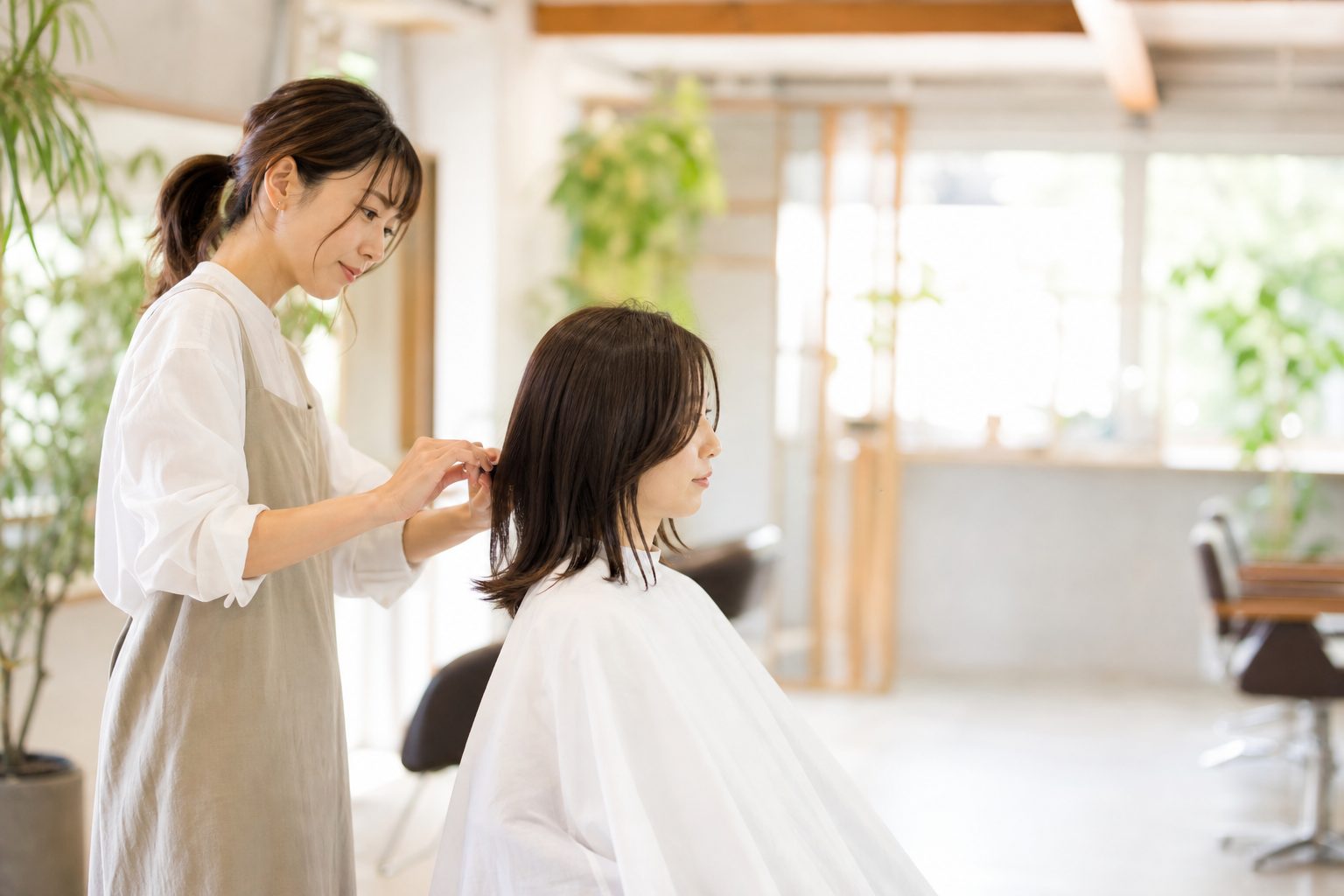 明るい店内で、髪の状態を確かめながら施術するスタイリスト